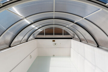 An empty fiberglass swimming pool with a sliding polycarbonate cover on a sunny spring day. A pool is white-colored, while the pavilion is half-transparent with blue toning.