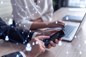 Two HR specialists in formal wear analyzing the market using phone to find new interns for recruitment program at international consulting company. Social networking and media hologram icons.