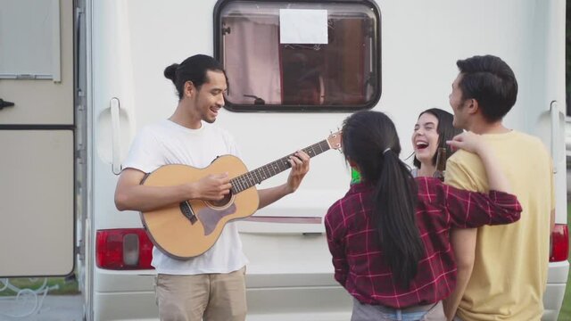 Group of friends playing guitar and singing a song at outdoor party.