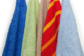 Colored terry bath towels hanging on a white background, fragment