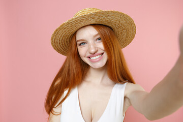 Young smiling caucasian cheerful nice redhead woman 20s ginger long hair wearing straw hat summer clothes doing selfie shot on mobile phone isolated on pastel pink color background studio portrait.