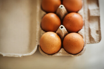 A cardboard box of brown chicken eggs from the store sits on the kitchen table, illuminated by the light. Food for breakfast.