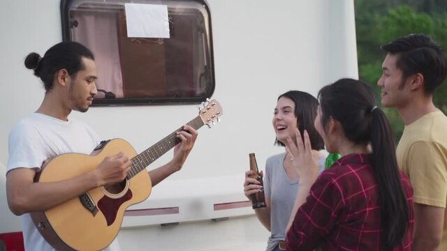 Group of friends playing guitar and singing a song at outdoor party.