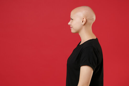 Side profile view of young bald caucasian attractive woman 20s without hair with alopecia problem wearing black basic casual t-shirt looking aside isolated on red color background studio portrait.