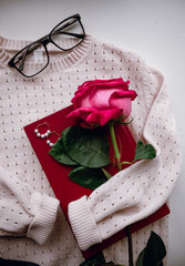 women's beige pullover lies on a white background with a red book, jewelry and a rose