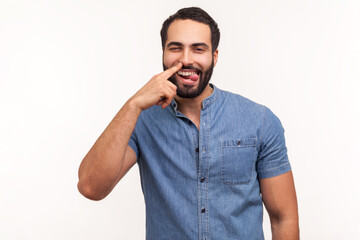 Funny comical man with beard picking finger to nose and showing tongue, looking at camera with smile, having fun, fooling around, bad manners. Indoor studio shot isolated on white background