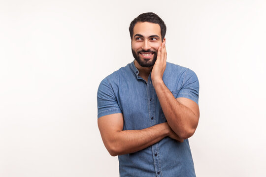 Smiling positive bearded man in blue shirt leaning head on hand, dreaming about future, fantasising and planning his weekend, visualization. Indoor studio shot isolated on white background