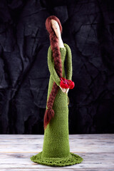 Textile handmade doll in green dress with brown long braids and scarlet flower