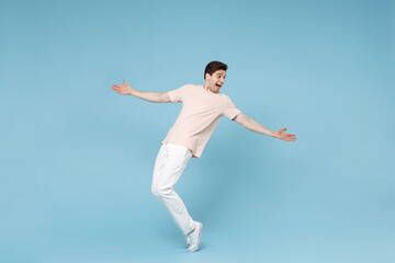 Fototapeta na wymiar Full length of young caucasian attractive smiling student man 20s in beige t-shirt white pants leaning over with outstretched hands looking aside isolated on blue color background studio portrait