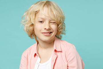 Funny cheerful little curly kid boy 10s years old wearing pastel pink shirt blinking looking camera...