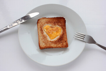 Toast bread with frighten egg in a heart shaped hole on plate on white background. Creative Valentine's day or Mothers day breakfast idea