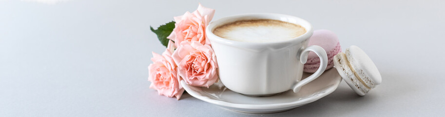 Cup of coffee, pasta for the cake and pink roses on a gray background. Copy space. Banner