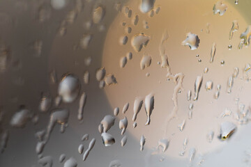 Raindrops are flowing down the glass on the window. Glare and sideways from lamps