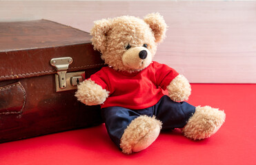 Suitcase and teddy bear on red floor. Retro leather bag in a kid room