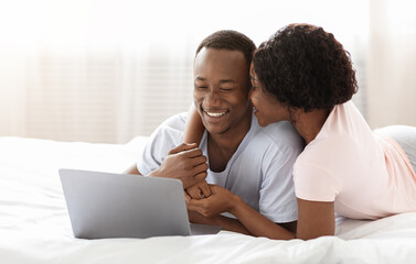 Fototapeta premium Romantic black man and woman using laptop in bed