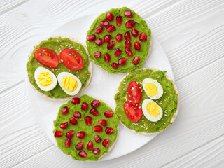 Rice cakes with avocado mash and eggs with tomato and pomegranate seeds in white plate