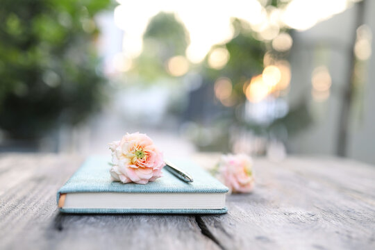 Soft Pink Roses And Notebook And Pencil On Wooden Table