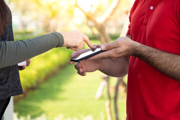 Signing signature on smart phone device to get a package. Beautifu woman receiving package from delivery man in red uniform at home.