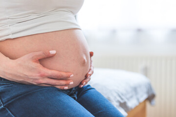 Happy pregnant in blue jeans mother is hugging her naked tummy, close up