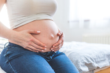 Happy pregnant in blue jeans mother is hugging her naked tummy, close up