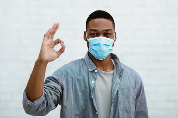 African Guy Wearing Face Mask Gesturing Okay Over Gray Wall