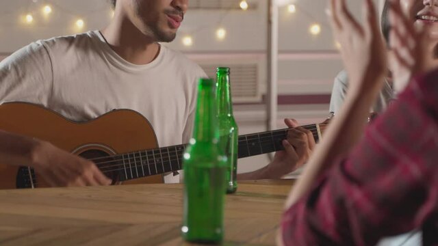 Friends are playing guitar, clapping their hands and singing at night.