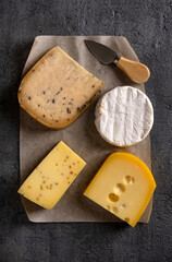 Various types of cheese on grey board. Dark moody. Top view. Closeup.