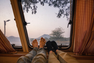 Legs of young couple relaxing in camper van with mountain view on lakeside