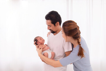 Asian or Hispanic father with beard hold his first child newborn with strong arm, beautiful wife play with baby and try to help husband hold the baby with carefully, happy new married couple with baby