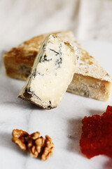 Slice of blue aged Stilton cheese accompanied with quince marmalade or jelly or jam Spanish dulce de Membrillo and walnuts on white marble tray. Selective focus