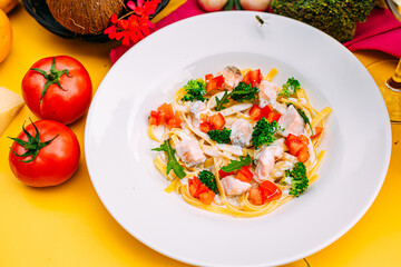 spaghetti with salmon, broccoli and tomatoes in a creamy sauce on a decorated table