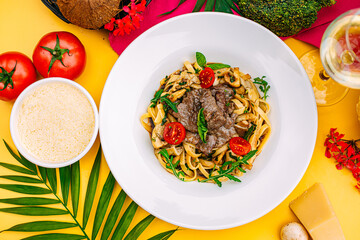 Fetuccini with fried meat and tomatoes on a decorated table