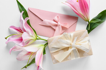 Beautiful lilies, gift and envelope on white background