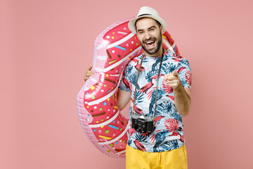 Cheerful young traveler tourist man in summer clothes hat hold inflatable ring pointing index finger camera on you isolated on pink background. Passenger travel on weekend. Air flight journey concept.