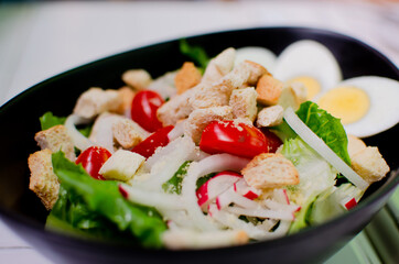 Caesar salad in black bowl cup with tomatoes, eggs and onion
