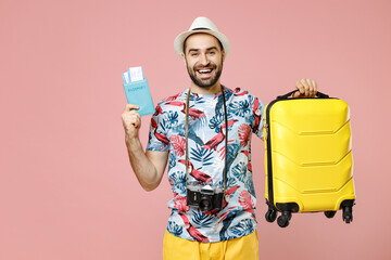 Cheerful young traveler tourist man in summer clothes hat photo camera hold suitcase passport ticket looking aside isolated on pink background. Passenger travel on weekend. Air flight journey concept.