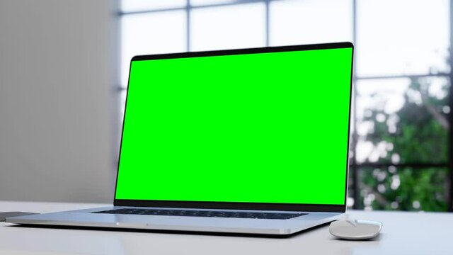 Laptop with blank green screen in office interior. Smooth camera movement around object with bokeh background. Home interior or office, 4k 24fps UHD
