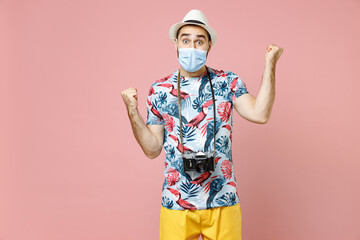 Fototapeta na wymiar Happy young traveler tourist man in face mask safe from coronavirus virus covid-19 clenching fists like winner isolated on pink background. Passenger traveling on weekend. Air flight journey concept.