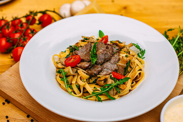 Fetuccini with fried meat and tomatoes on a decorated table