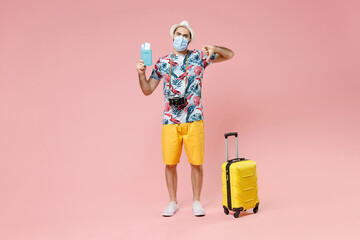 Full length displeased traveler tourist man in mask safe from coronavirus hold passport tickets showing thumb down isolated on pink background. Passenger travel on weekend. Air flight journey concept.