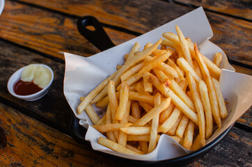 French fries on white paper wrap, with mayonnaise and ketchup. Wood table background
