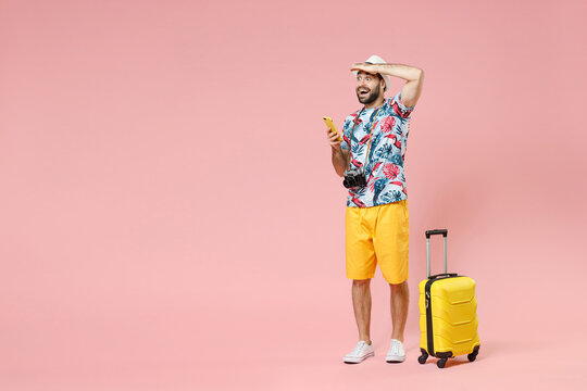 Full length of excited young traveler tourist man using mobile phone booking hotel taxi looking far away distance isolated on pink background. Passenger travel on weekend. Air flight journey concept.