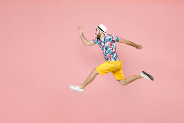 Full length side view shocked young traveler tourist man in summer clothes hat jumping spreading hands running isolated on pink background. Passenger traveling on weekend. Air flight journey concept.