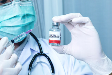 Doctor wear medical gloves hand holding vaccine bottle COVID-19 infection on blue background. Coronavirus Covid-19 vaccination concept.