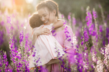 Young beautiful mother and her little daughter outdoors with flowers. Violet field of flowers and people there