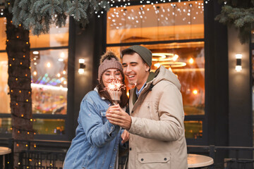 Happy young couple with Christmas sparklers outdoors on winter day