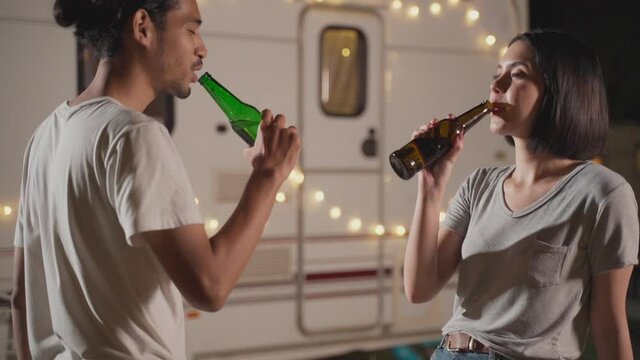 Lovely asian couple clinking, drinking bottles of beer and smiling.
