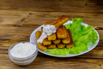 Fried fish fingers on a plate with lettuce and tartar sauce on wooden table