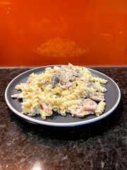 fusilli pasta with white cream sauce with mushrooms and bacon on a gray plate with orange background vertical