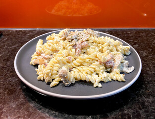 fusilli pasta with white cream sauce with mushrooms and bacon on a gray plate with orange background